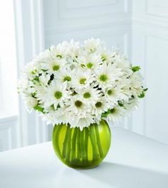 a green vase filled with white flowers on top of a table