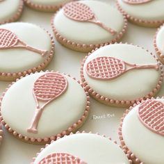 cookies decorated with pink and white icing are arranged on a table to look like tennis racquets