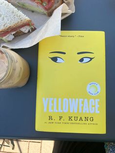 a yellow book sitting on top of a blue table next to a sandwich and drink