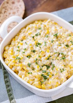 a white casserole dish filled with corn and parsley on a green towel