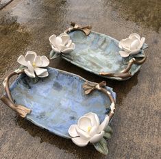 two ceramic trays with white flowers on them sitting in the rain, next to each other