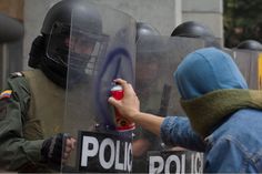 a group of people standing around each other with police in the background and one person holding a bottle