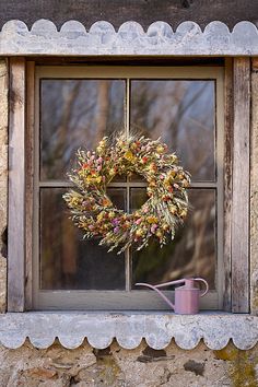 a wreath on the window sill next to a watering can