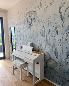 a white desk sitting in front of a window next to a wall with flowers on it