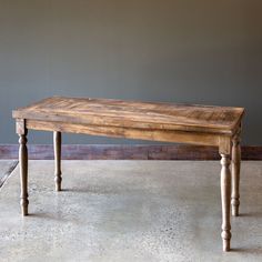 a wooden table sitting on top of a cement floor next to a gray painted wall