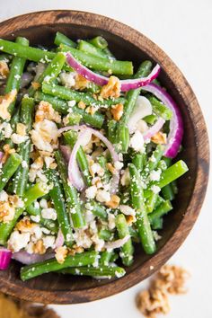 a wooden bowl filled with green beans, onions and feta cheese on top of it