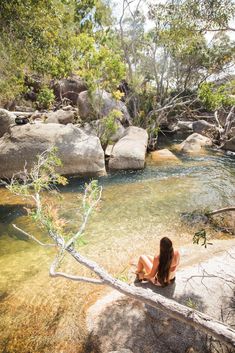 a woman is sitting on the rocks near a river