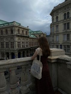 a woman standing on top of a balcony next to tall buildings