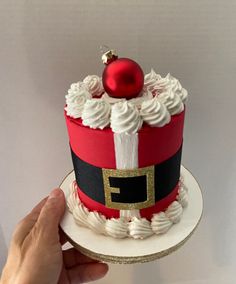 a hand holding a red and black cake with white frosting on top, topped with a santa hat