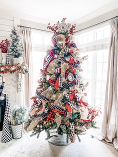 a christmas tree decorated with red, white and blue ribbons in a living room area