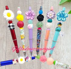 several pens are lined up on a wooden surface with flowers and beads attached to them