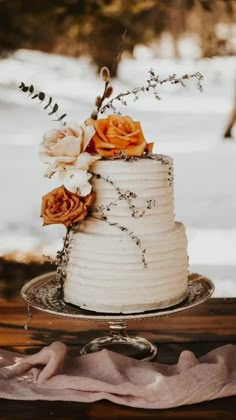 a white wedding cake with flowers on the top is sitting on a table in front of some snow