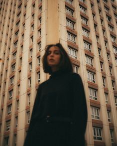 a woman standing in front of a tall building with lots of windows on the side