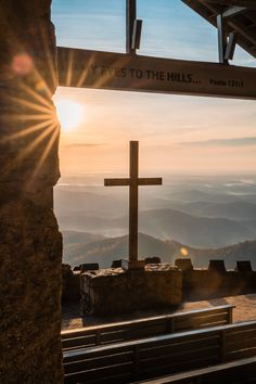 the sun shines brightly behind a cross at the top of a hill with mountains in the background