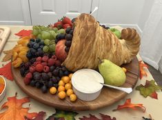 an assortment of fruits and croissants on a wooden platter next to a bowl of yogurt