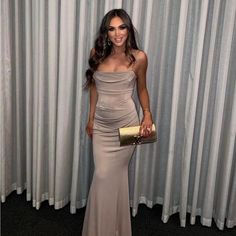 a woman standing in front of a curtain wearing a dress and holding a gold purse