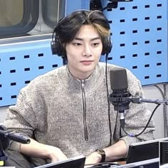 a young man sitting in front of a microphone with headphones on and looking at the camera