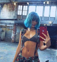 a woman with blue hair is looking at her cell phone while standing in an industrial area