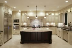 a large kitchen with an island in the middle and lights above it, along with two refrigerators