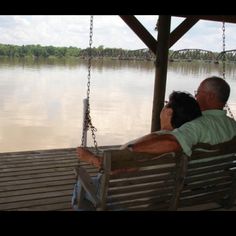 a man and woman sitting on a swing by the water