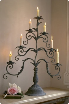 a metal christmas tree with lit candles on a table in front of a white wall