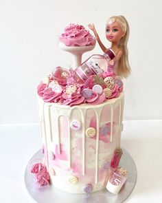 a barbie doll sitting on top of a pink and white cake with lots of candies