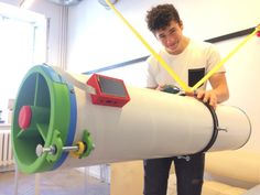 a young man standing next to a large white tube with a green and red device on it