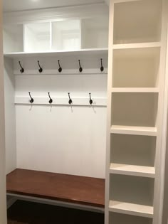 an empty room with white shelves and black hooks on the wall next to a wooden bench