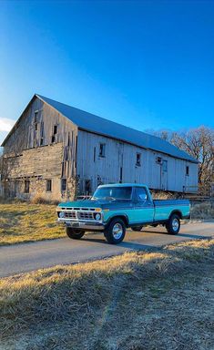 a blue pick up truck parked in front of an old barn