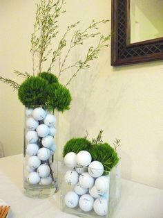 two vases filled with plants and balls on top of a white tablecloth covered table