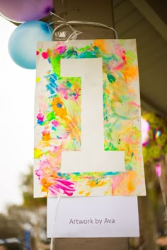 a sign that is hanging from the side of a building with balloons in the background