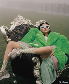 a woman sitting on top of a chair covered in a green blanket and wearing sunglasses