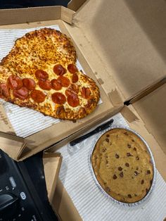 two pizzas in boxes with one slice missing and the other half eaten, sitting next to a cookie