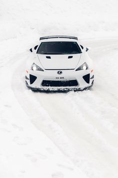 a white sports car driving down a snow covered road in the middle of wintertime