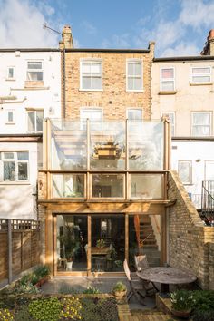 an outside view of a house with wooden decking and glass walls, surrounded by brick buildings