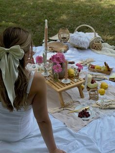 a woman sitting at a picnic table with food and drinks on the ground in front of her