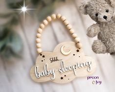 a teddy bear hanging from a wooden sign that says baby sleeping on it's side