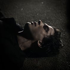 a young man laying on the ground with his head down and eyes closed looking up