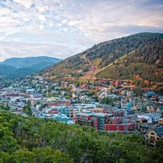 a view of a city in the mountains with trees and bushes around it, looking down on some buildings