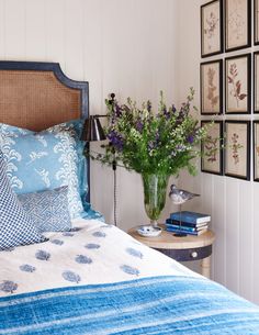 a bed with blue and white sheets, flowers in a vase on the end table