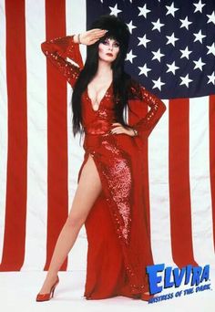 a woman in a red dress standing next to an american flag with her hands on her head