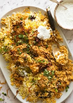 a white plate topped with chicken and rice next to a bowl of yogurt