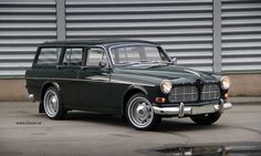 an old green station wagon is parked in front of a garage door and metal wall