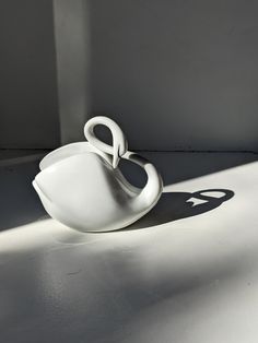 a white vase sitting on top of a table next to a shadow from the wall