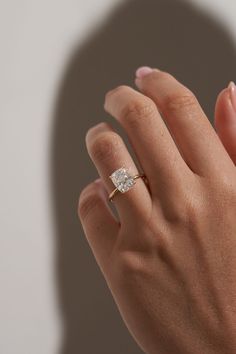 a woman's hand with a diamond ring on top of her finger, in front of a shadow