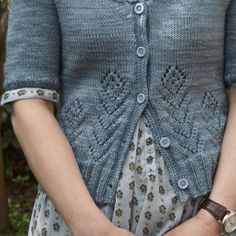 a close up of a person wearing a blue cardigan and holding their hands together