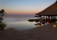 an outdoor swimming pool with chairs and umbrellas on the deck overlooking the ocean at sunset