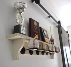 a shelf with baseballs, trophies and other items on it in a room that has white walls