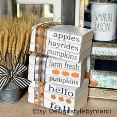 stacked books with pumpkins, apples and hay on them next to a potted plant