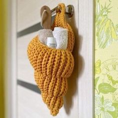 a crocheted towel holder hanging on a door with two rolls of toilet paper in it